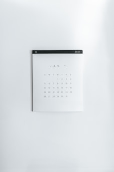 A simple wall calendar displays the month of January 2020 with dates arranged in a grid format. The calendar has a minimalistic design on a plain white wall, featuring a black strip across the top with the year '2020' printed on it.