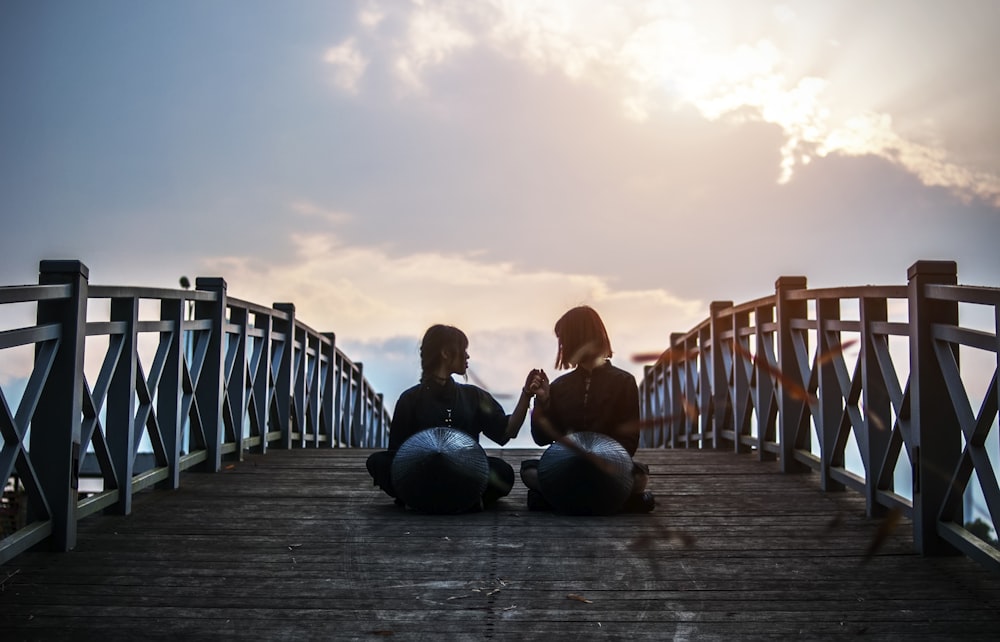 two person sitting on brown bridge