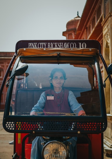 A friendly driver standing beside a clean, comfortable taxi with Jaipur's iconic architecture in the background.