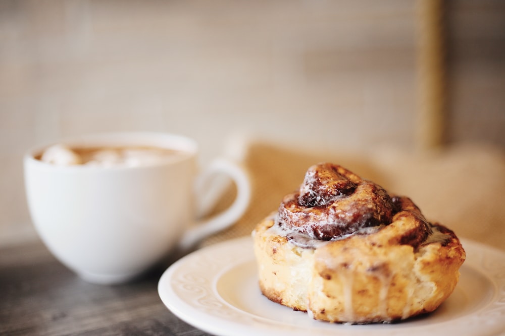 baked bread in plate beside cappuccino