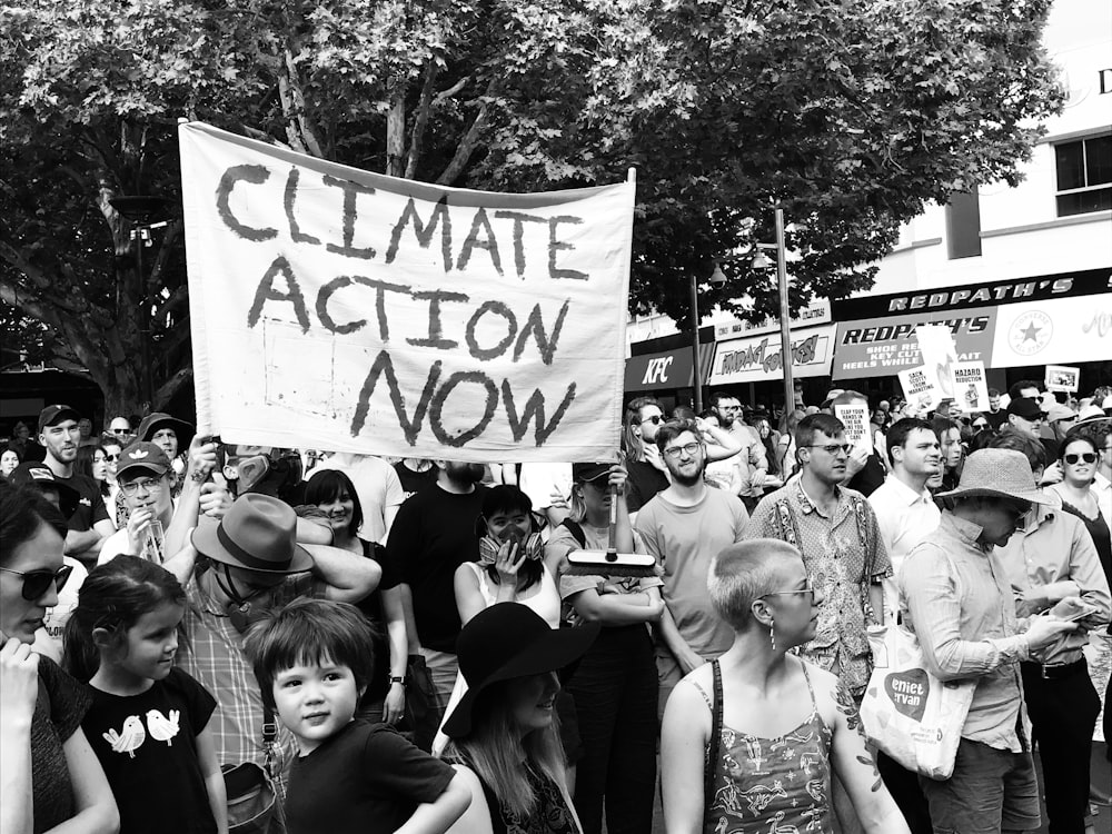 grayscale photo of people protesting on street while raising climate action now banner