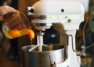 person pouring egg yolks on white stand mixer