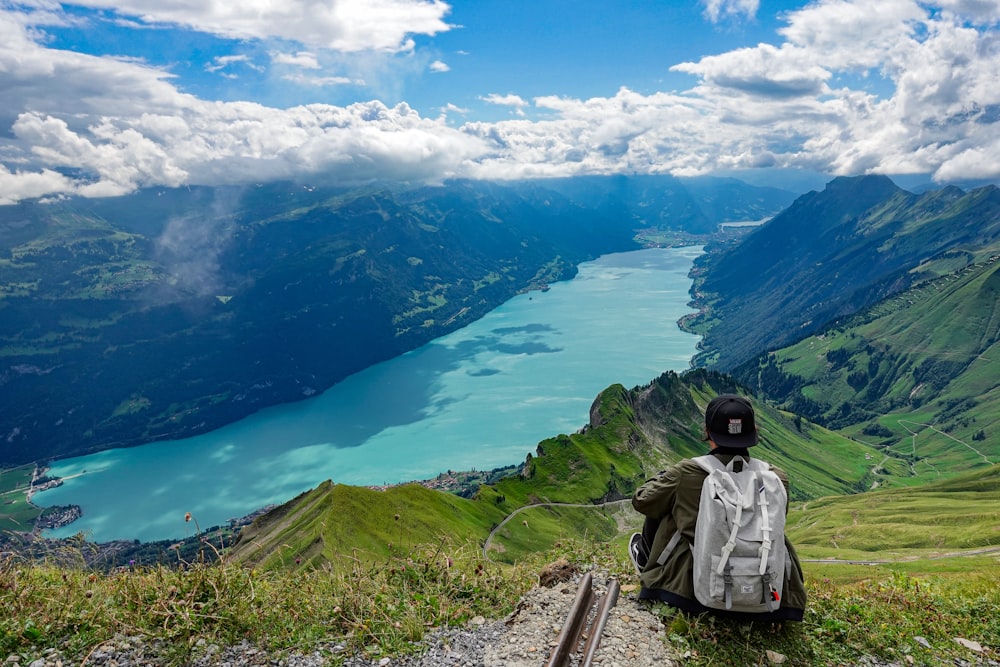 Person, die auf einer Klippe mit Blick auf Tal und Fluss unter blauem, bewölktem Himmel sitzt