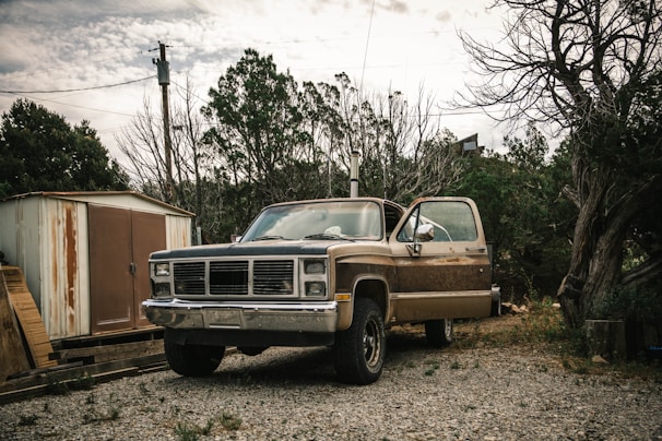 Hank revving up his rusty old pickup truck with a cheeky grin under a corrugated metal carport
