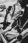 A close-up view of a motorcycle engine featuring shiny chrome parts that reflect the surroundings, including clouds and nature in the background. The intricate mechanical components are clearly visible, with a strong focus on the circular element at the center.