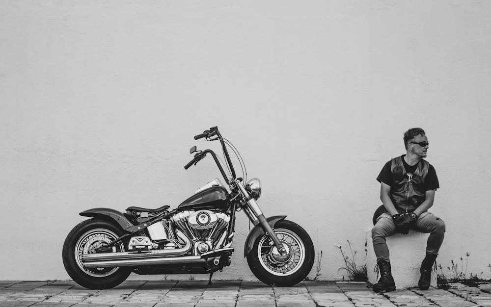 Una foto in bianco e nero di un uomo seduto accanto a una motocicletta