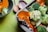 A close-up of a baking tray filled with fresh vegetables including broccoli florets and orange pumpkin slices, with foil wrapped around the pumpkin. A green bowl containing broccoli and wooden spoons can also be seen in the background on a green surface.
