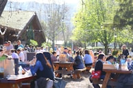 Families and friends gathered around picnic tables enjoying local food and drinks under string lights.