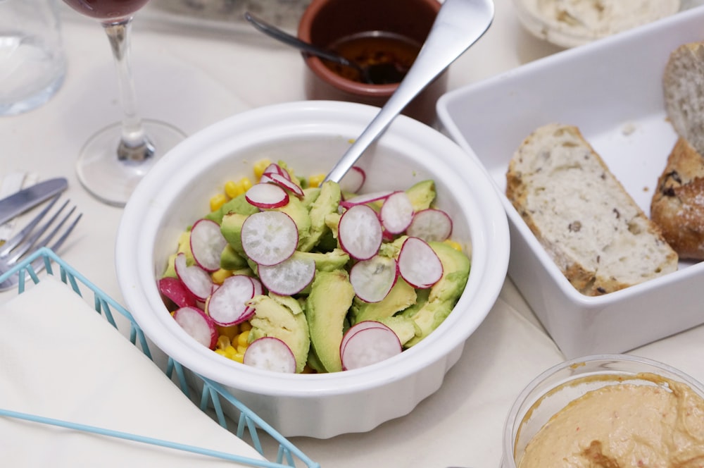 sliced vegetables in bowl beside breads