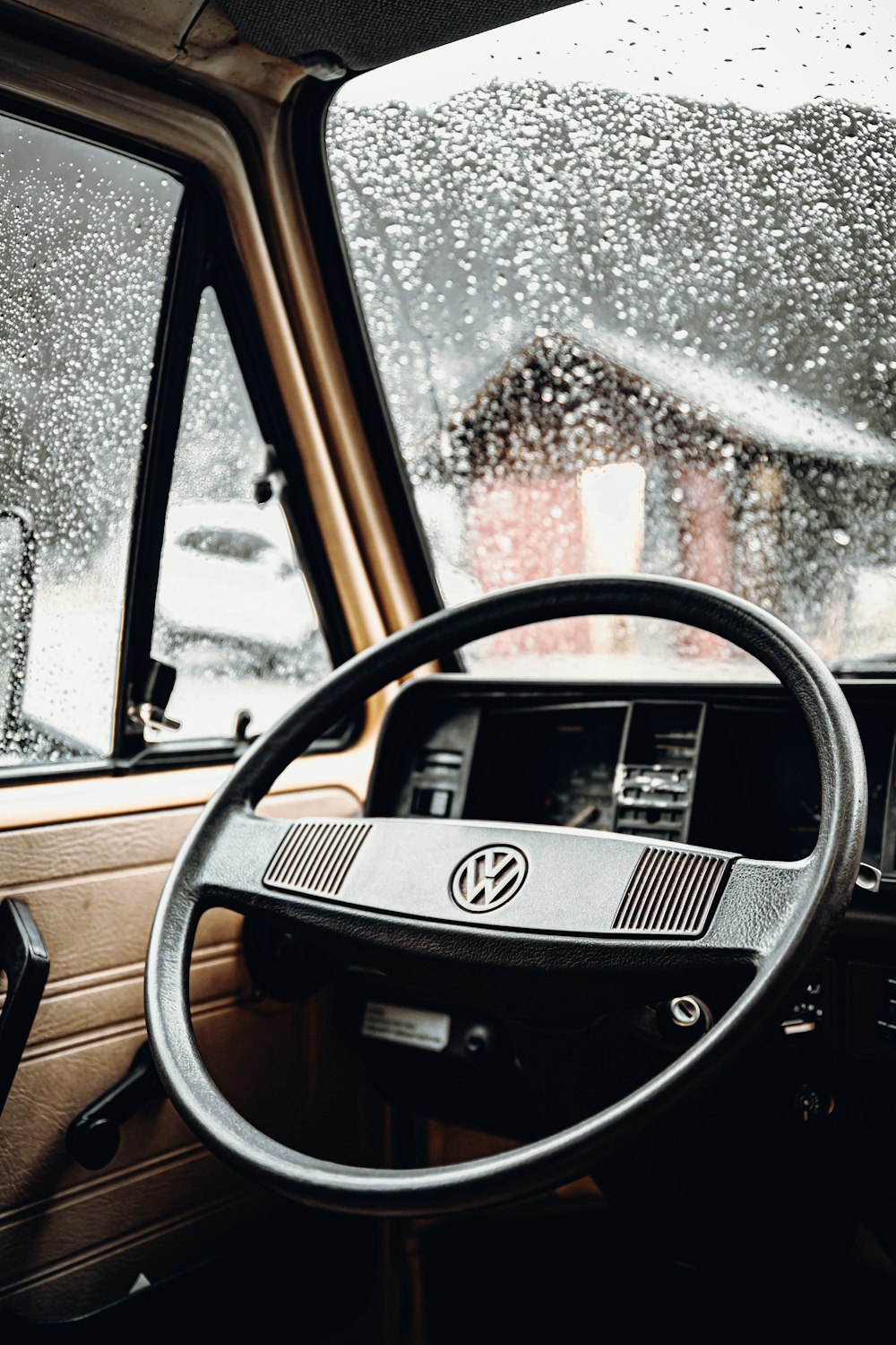 a steering wheel and dashboard of a vehicle on a rainy day