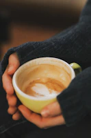 Hands holding a warm cup of coffee with a honey dipper resting beside it.