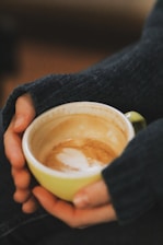 A cozy scene showing a hand holding a beautifully designed ceramic cup filled with steaming coffee.