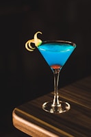 blue drink in wine glass on corner of wooden table