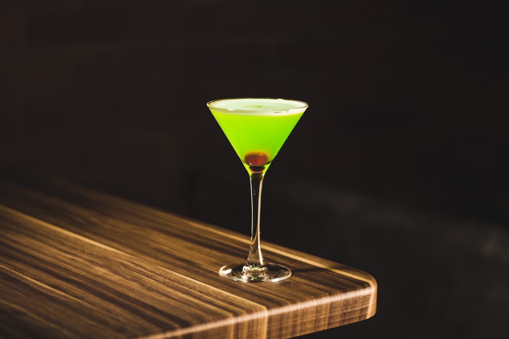 green drink in wine glass on corner of wooden table