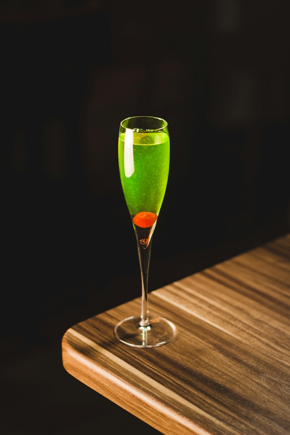 green drink-filled tulip glass on corner of wooden table