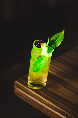 A vibrant tropical cocktail in a glass garnished with fresh mango slices and mint leaves on a sunny wooden table.