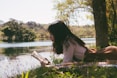 Une femme allongé au bord d'un cours d'eau durant une belle journée, en train de lire
