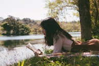 Une femme allongé au bord d'un cours d'eau durant une belle journée, en train de lire