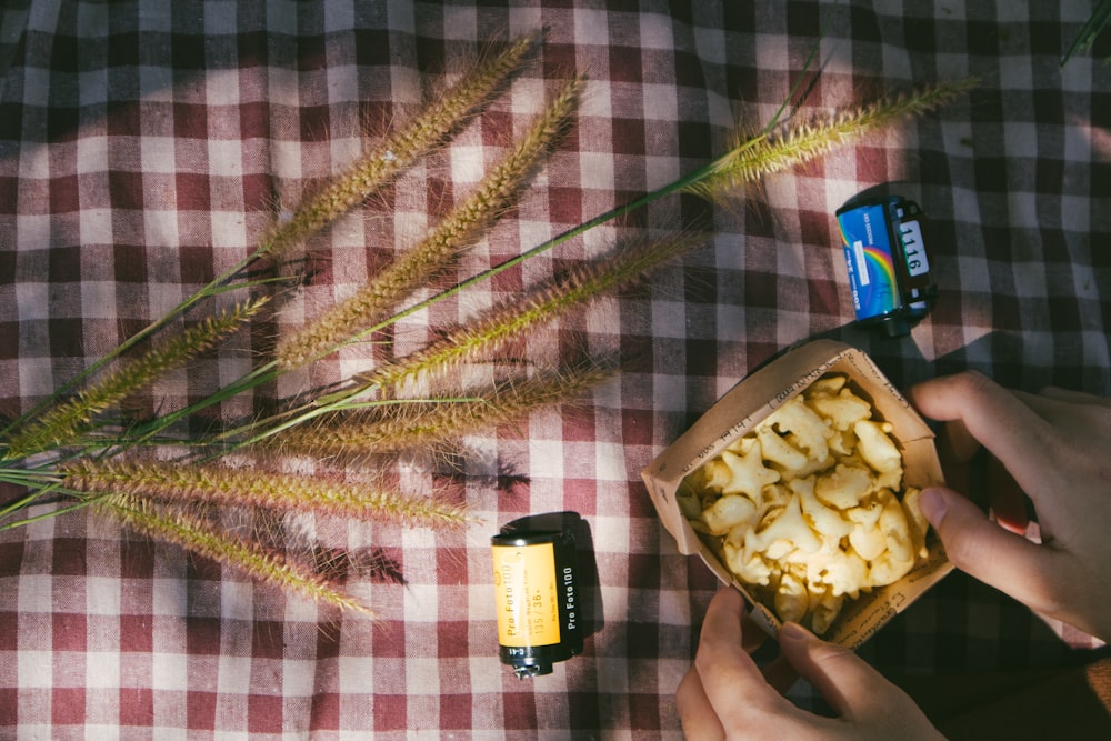 person holding small box with biscuits inside and brown cluster plant near camera film