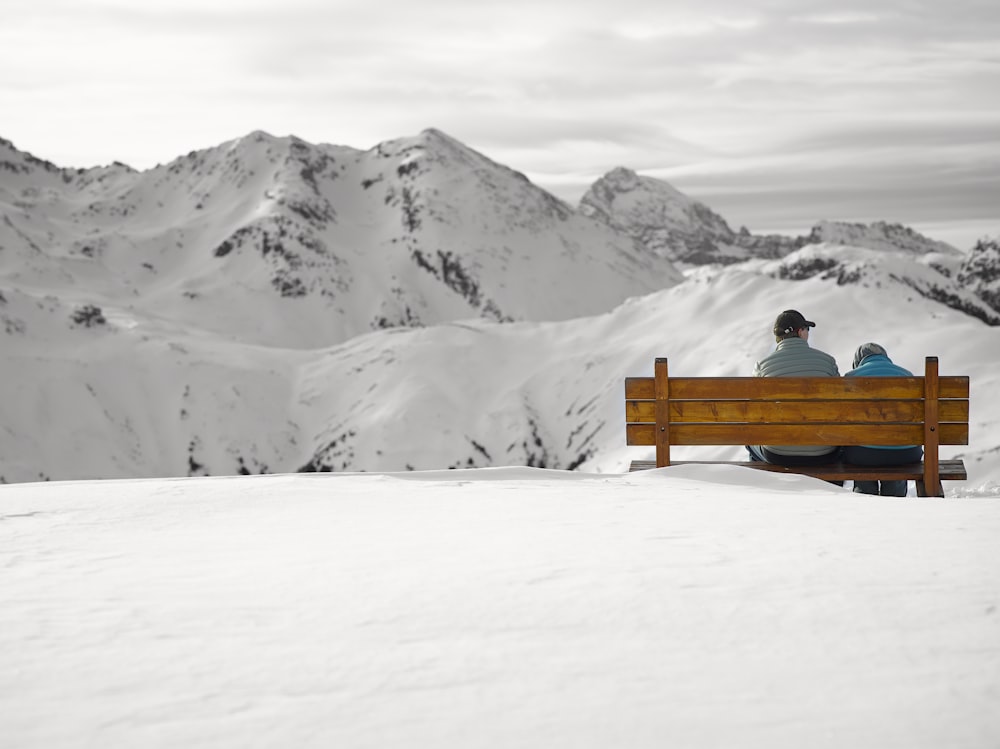 Dos personas sentadas en un banco en un campo de nieve frente a las montañas glaciares