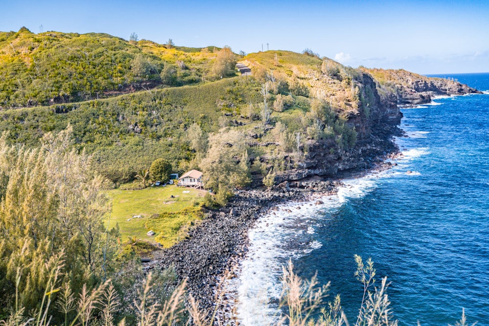 landscape photography of houses on green field viewing cliff and body of water under white and blue sky