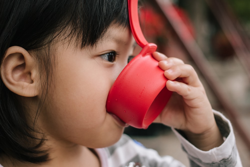 Foto Niño con chaqueta gris bebiendo con taza roja – Imagen Humano gratis en