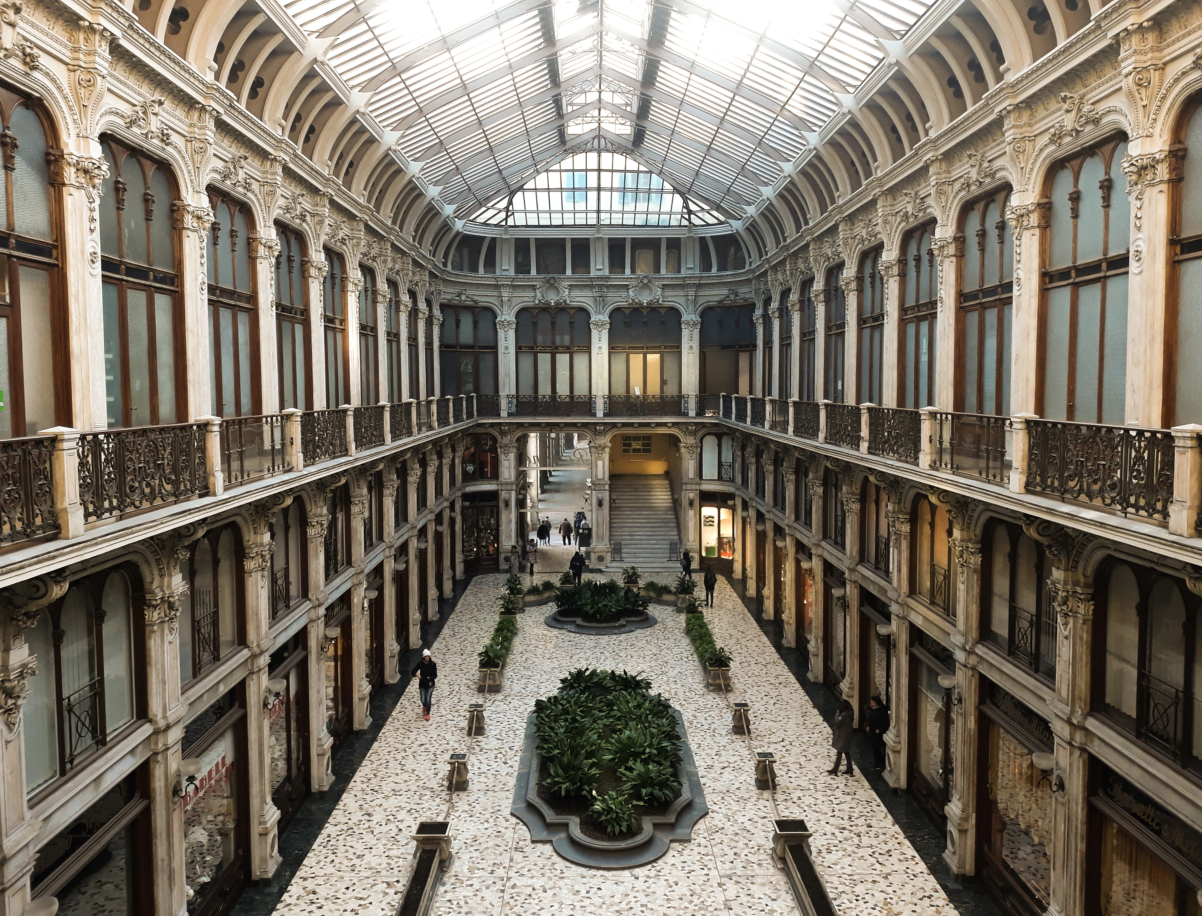 A grand glazed 19th-century arcade with tiered iron balconies around a central garden courtyard.