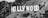 A large, iconic sign featuring the word 'HOLLYWOOD' in bold, white capital letters is mounted on a hillside. The surrounding terrain includes rugged, grassy hills with scattered shrubs and small trees. The entire scene is presented in black and white.