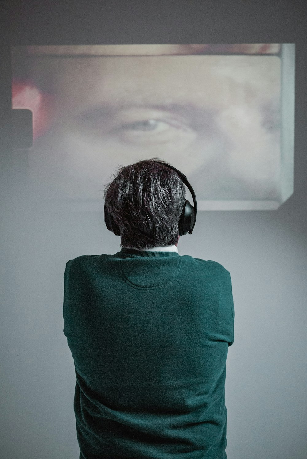 person wearing green shirt using black headphones while standing and facing back and watching movie