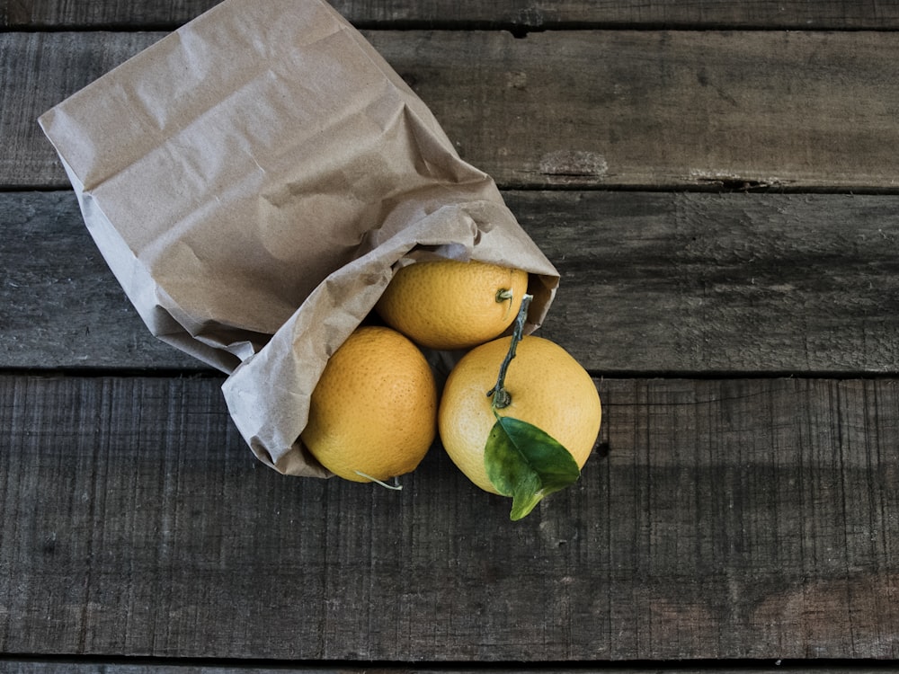 three yellow citrus fruits in brown paper bag