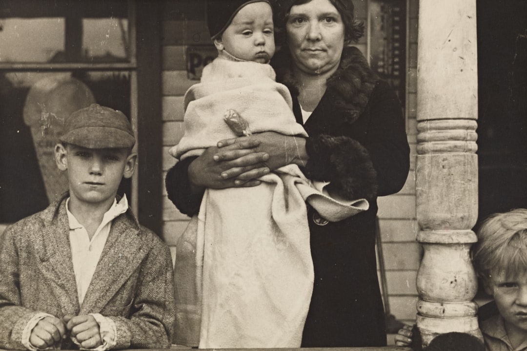 grayscale photography of woman holding baby covered with blanket beside boy