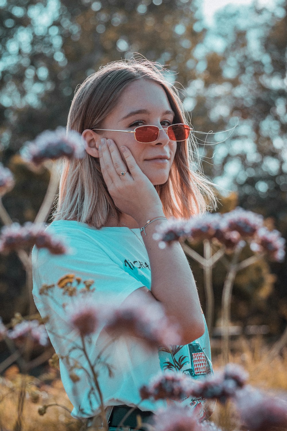 a girl wearing sunglasses standing in a field of flowers