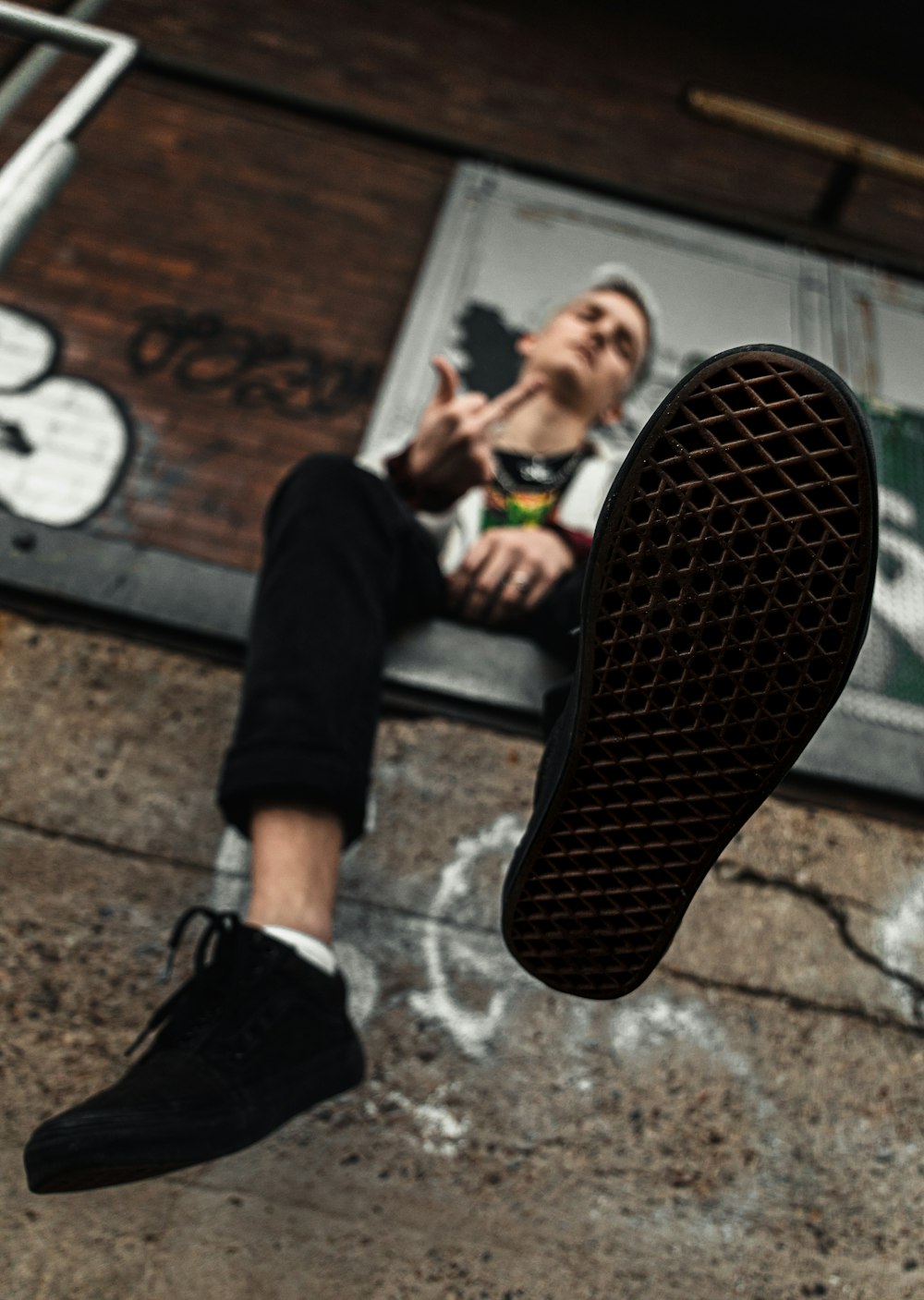 man wearing black and multicolored crew-neck shirt, black jeans, and black sneakers sitting and making finger sign