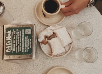 black coffee in white ceramic mug near sliced cake, water in drinking glass, and clear condiment shaker on table