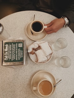 A rustic wooden table at Beignet Station piled high with powdered sugar-dusted beignets and a steaming cup of chicory coffee.