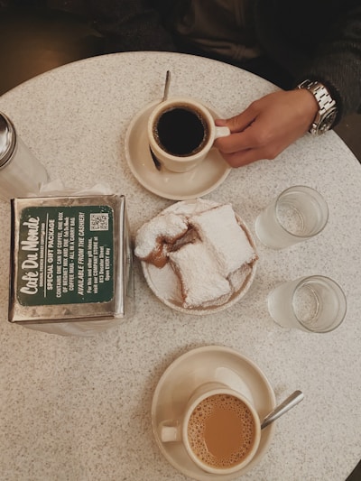 A rustic wooden table at Beignet Station piled high with powdered sugar-dusted beignets and a steaming cup of chicory coffee.