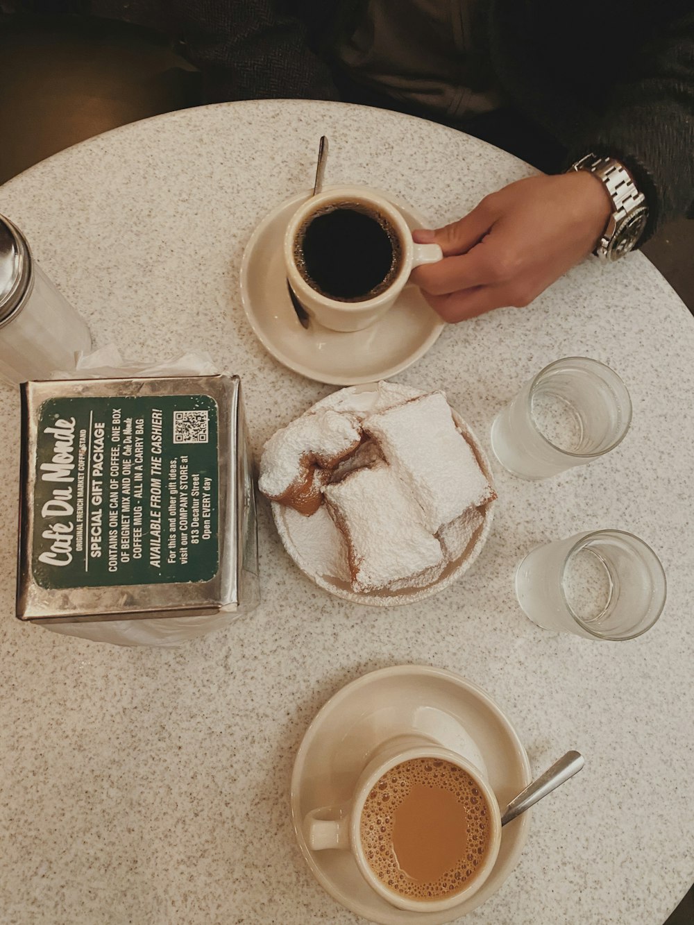 얇게 썬 케이크 근처의 흰색 세라믹 머그잔에 담긴 블랙 커피, 음료수 잔에 담긴 물, 테이블 위의 투명한 조미료 셰이커