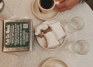 black coffee in white ceramic mug near sliced cake, water in drinking glass, and clear condiment shaker on table