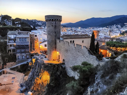 A cozy medieval village with players interacting around a campfire at sunset.