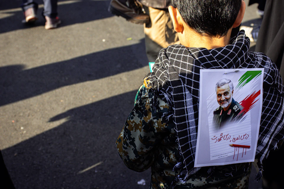 Young boy wearing camouflage jacket carries white paper with man's face image in background