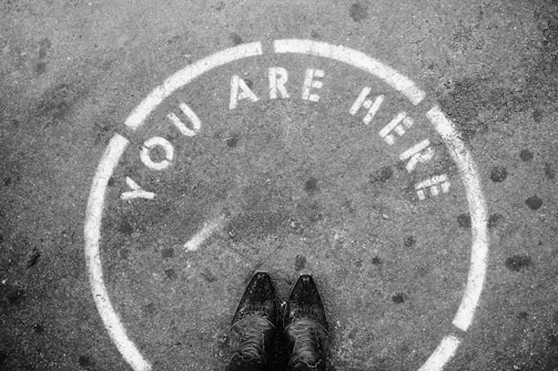 person wearing black leather shoes with a circle around her saying "You are here"