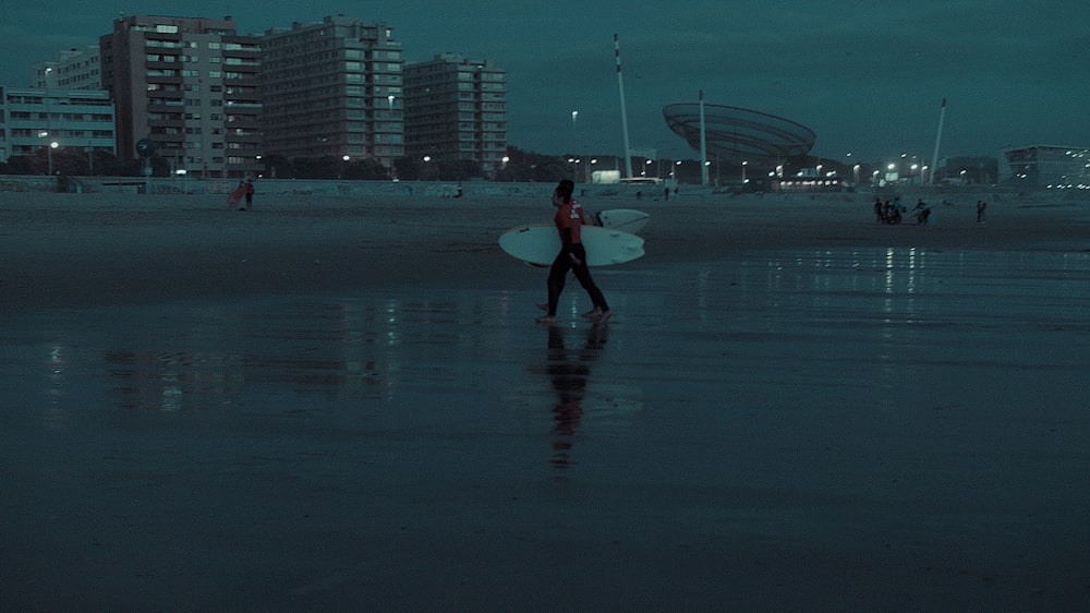 person walking on seashore holding surfboard at night