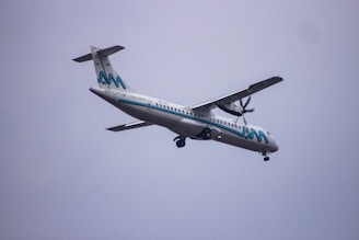 A propeller-driven passenger airplane, branded with the name Aeromar, is flying through a cloudy sky. The aircraft is white with blue and black accents, featuring a logo on the tail and the company name along the fuselage.