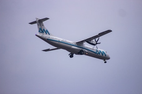 A propeller-driven passenger airplane, branded with the name Aeromar, is flying through a cloudy sky. The aircraft is white with blue and black accents, featuring a logo on the tail and the company name along the fuselage.