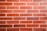 A close-up of a red brick wall with uniform rectangular bricks. The bricks are arranged in a staggered horizontal pattern with light-colored mortar in between.