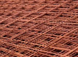 A close-up view of overlapping metal grids or steel meshes, displaying a complex lattice pattern with intersecting lines and a slightly rusted texture.