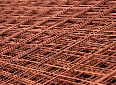 A close-up view of overlapping metal grids or steel meshes, displaying a complex lattice pattern with intersecting lines and a slightly rusted texture.