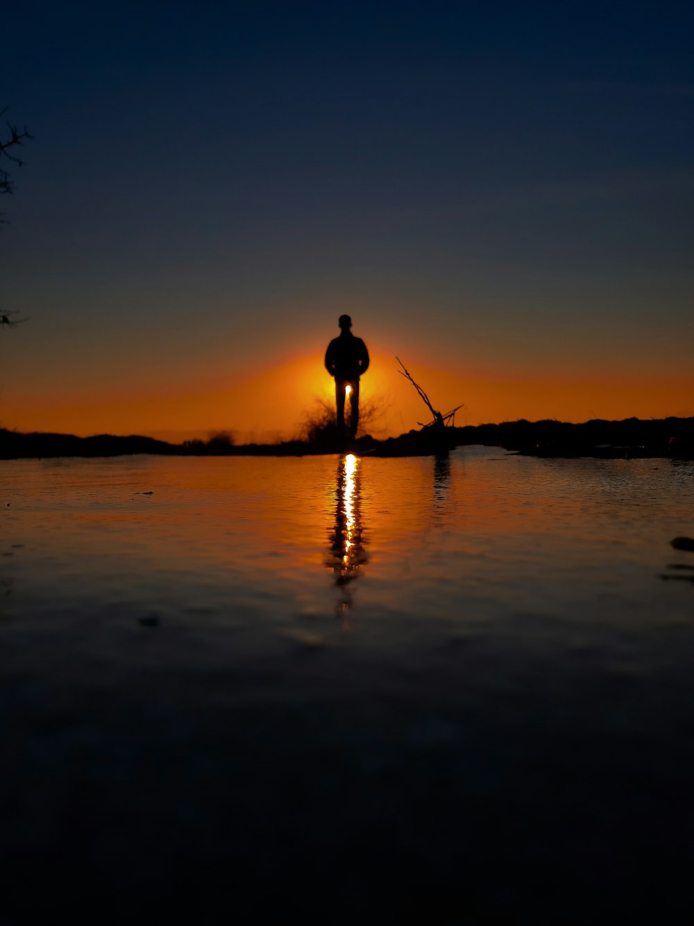 silhouette of man standing on water during sunset