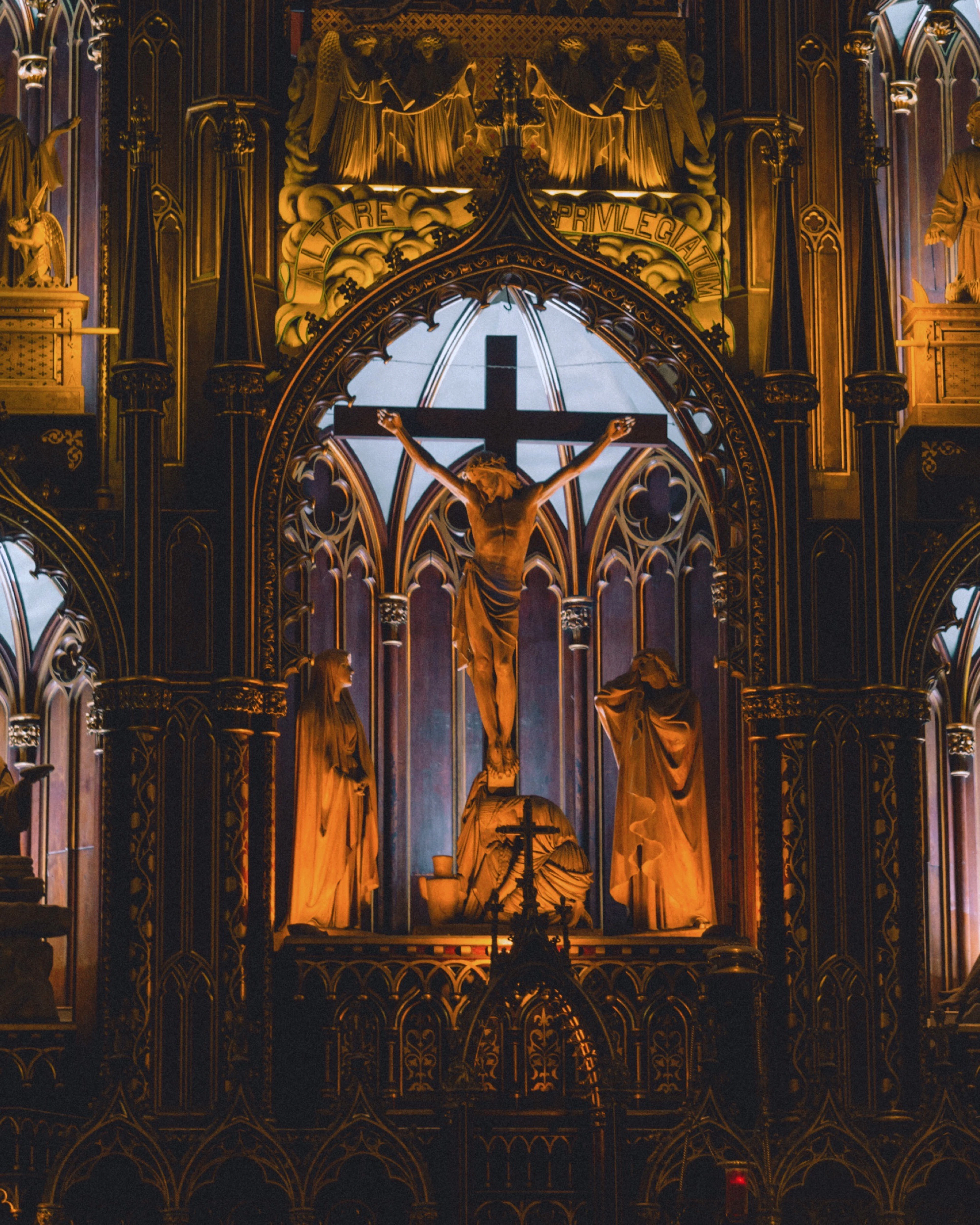 A gilded crucifix and mourning statues are lit in warm gold inside a carved wooden altarpiece.