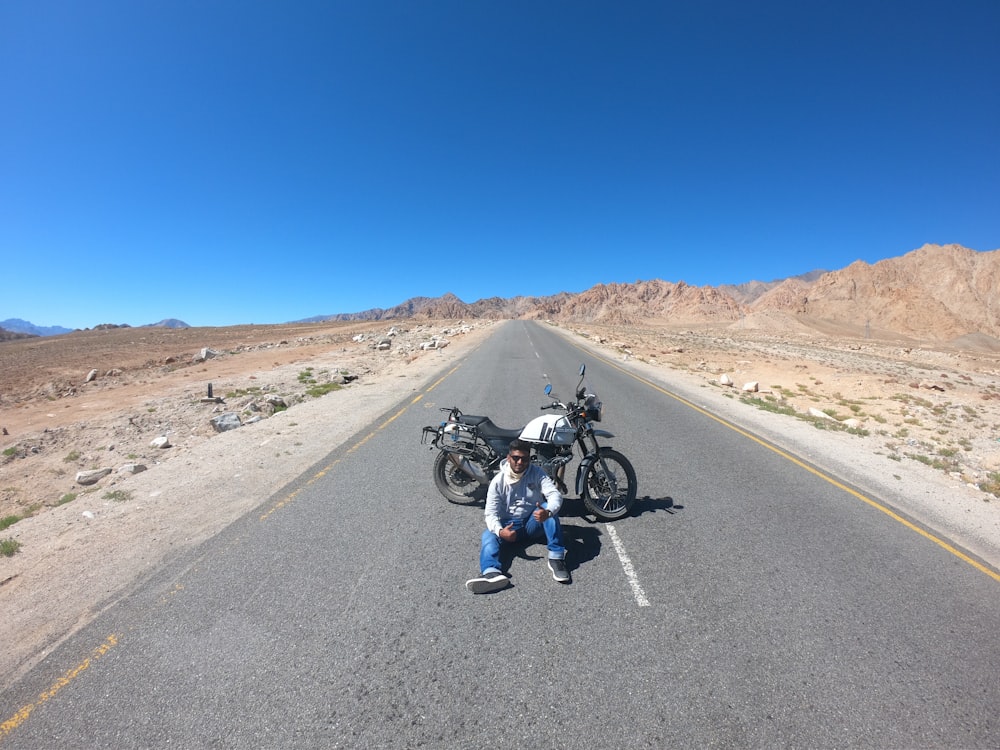 Hombre sentado en la carretera cerca de la motocicleta durante el día